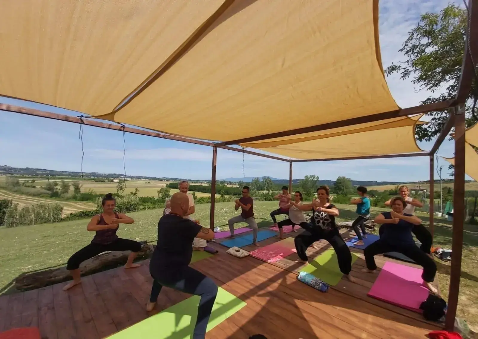 Gruppo durante una pratica yoga all’aperto su una pedana affacciata sulla campagna
